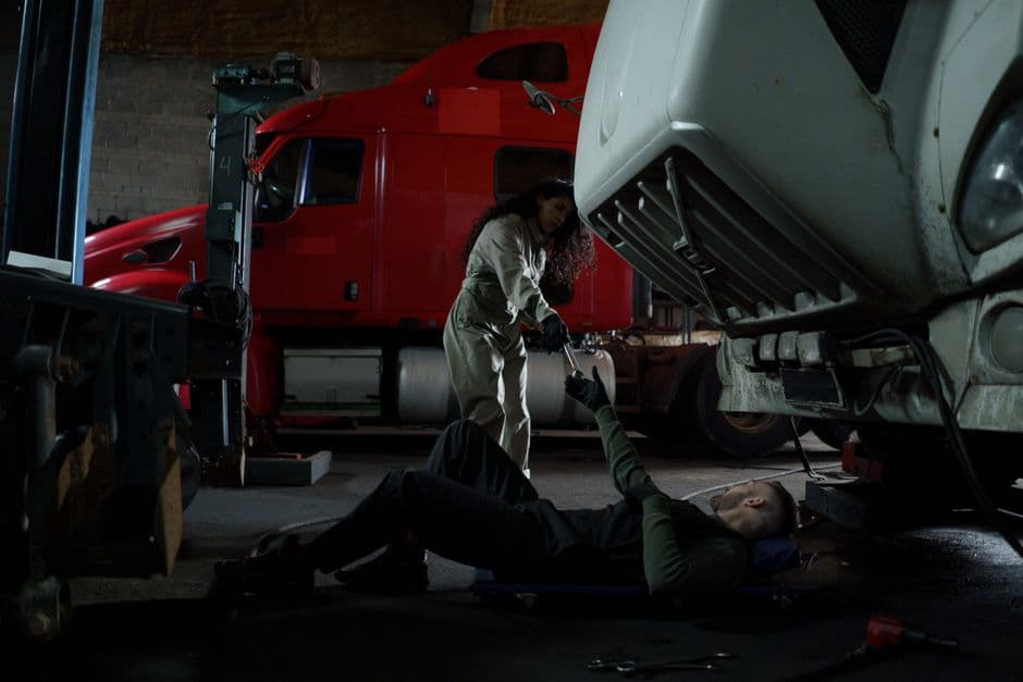 Two mechanics working together to repair a truck in a dimly lit garage setting